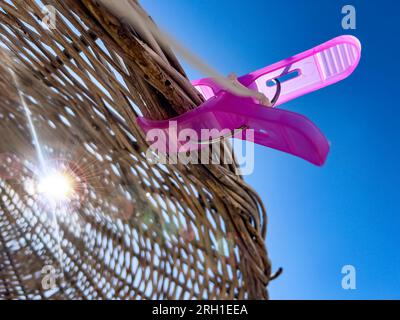 Große rosa Kleidernadel am Strohschirm aus Rattan am Strand. Sonnenstrahl fällt an sonnigen Tagen durch einen exotischen Sonnenschirm. Hintergrund der Sommeraktion Stockfoto