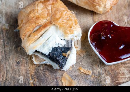 Blätterteig-Brötchen aus Weizenteig und Mohnsaatfüllung, ein Brötchen mit süßer Mohnsaatfüllung auf dem Tisch Stockfoto