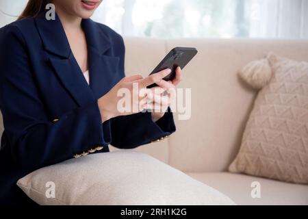 Nahaufnahmen einer asiatischen Geschäftsfrau, die ein Smartphone für soziale Medien verwendet, online auf dem Sofa zu Hause sitzt, Geschäftsfrau, die wie ein cleveres Telefon aussieht Stockfoto