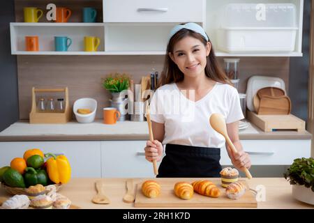 Glück wunderschöne junge asiatische Frau in der Schürze lächelt während sie Essen zubereitete, während sie sich zu Hause in der Küche entspannt, Porträt weibliches Frühstück zubereitete Stockfoto
