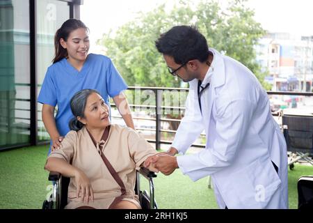 Pflegende asiatische Frau und Arzt Pflege ältere auf Rollstuhl sitzend, trösten für die Förderung im Garten im Krankenhaus, Seniorentherapie und Rehabilitation Stockfoto