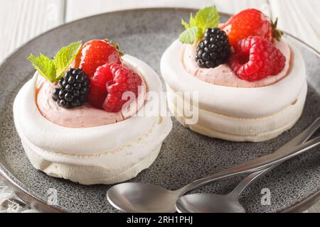 Mini-Pavlova-Kuchen mit Himbeerdewberry-Erdbeere mit Sahne und Pfefferminz, geschlossen auf einem Teller auf dem Holztisch. Horizontal Stockfoto