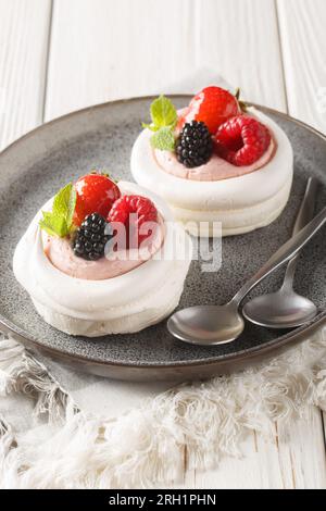 Erdbeeren, Taubeeren, Himbeeren und Sahne schmücken Anna Pavlova Kuchen auf einem Teller auf dem Holztisch. Vertikal Stockfoto
