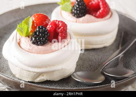 Hausgemachter Mini-Baiser-Pavlova-Kuchen mit Beeren und Schlagsahne auf einem Teller auf dem Holztisch. Horizontal Stockfoto