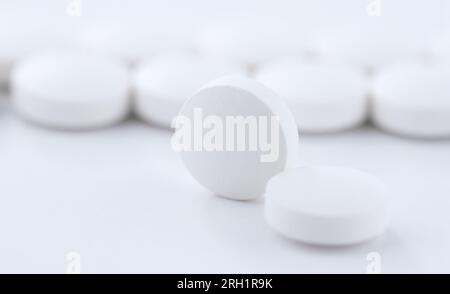 Nahaufnahme einer runden Pille vor dem Hintergrund von in einer Produktionslinie hintereinander gestapelten Tabletten. Stockfoto