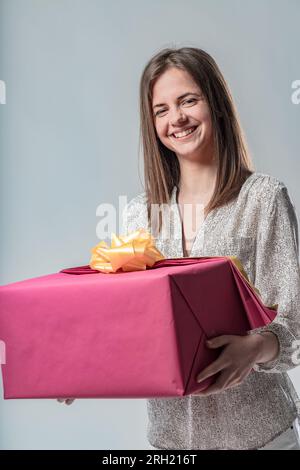 Glückliche Frau mit großem rot-lila Geschenk, gelbe Schleife, in einer eleganten Bluse, die nur schlanke Leute tragen können. Ein Geschenk könnte ihres oder ein Geschenk sein Stockfoto