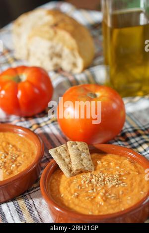 Spanisches Porra-Gericht. Vegetarisches Sommergericht, Tomatensuppe mit Sesamsamen und Crackern, auf einer Tonschale, mit Tomatos und Brot auf dem Backgroun Stockfoto