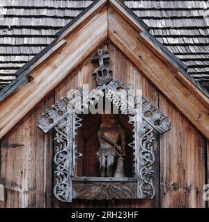 Die Figur Christi, gefesselt an den Pfosten, geschnitzt in Holz. In einer Giebelnische der Veranda auf der Südseite der Holzkirche von Ende 1400s, Dębno Podhalańskie, Polen. Stockfoto