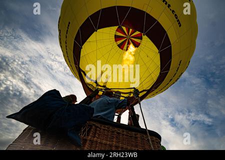 Heißluftballonpiloten testen die Brenner vor dem Flug, während Ballons am letzten Tag der Bristol International Balloon Fiesta in Ashton Court, Bristol, starten. Regen und feuchtes Wetter über das Wochenende haben die Ballons in den Himmel getrieben, da die Baumkronen nass wurden und Crews versuchten, sie abzutrocknen. Foto: Sonntag, 13. August 2023. Stockfoto