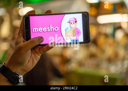 Frau, die ein Handy hält, das das Meesho-Logo des indischen Social Commerce-Startups auf einer Veranstaltung zeigt Stockfoto