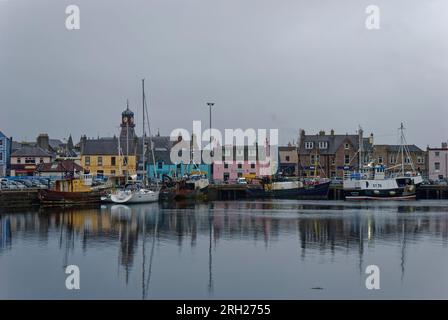 Farbenfrohe Gebäude säumen die Uferpromenade hinter den Fischerbooten, die neben den Steinkai von Stornoway in den Äußeren Hebriden festgemacht sind. Stockfoto