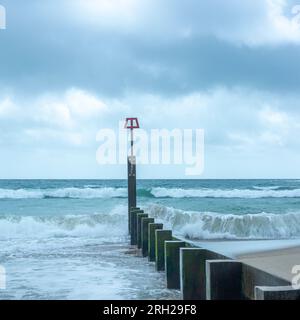 Wellen brechen an einem windigen Tag über einem Groyne Stockfoto