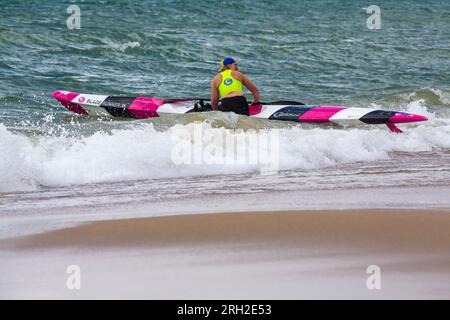 Branksome Chine, Poole, Dorset, Großbritannien. August 2023. Die Surf Life Saving GB National Surf Lifesaving Championships Masters Championships finden am Branksome Chine Beach statt. Der Wind und starke Wellen schaffen schwierige Bedingungen für die Konkurrenz. Rettungsschwimmer spielen eine wichtige Rolle am Meer und an der Küste mit ihren Fähigkeiten zur Rettung und Rettung. Frau, die Gaisford Blade Runner Xi Surf Ski im Meer bereit macht, um Surf Ski zu gehen Surf Skiing. Quelle: Carolyn Jenkins/Alamy Live News Stockfoto