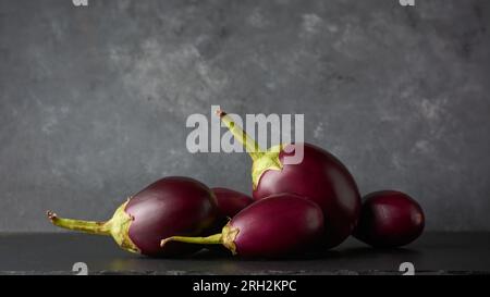 Seitenansicht von Auberginen oder Brinjalen auf schwarzer Tischplatte, auch als Aubergine bekannt, beliebtes tieflila Gemüse, das in verschiedenen Küchen auf schwarzen s verwendet wird Stockfoto