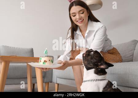 Junge Frau und ihre französische Bulldogge mit Kuchen, die den Geburtstag zu Hause feiert Stockfoto