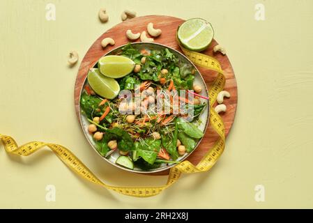 Teller mit frischem Salat und Maßband auf gelbem Hintergrund. Diätkonzept Stockfoto