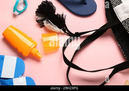 Flasche Sonnencreme mit Tasche und Flip Flops auf pinkfarbenem Hintergrund Stockfoto