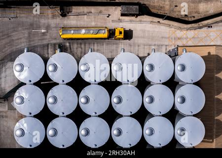 Luftaufnahme direkt über großen Lagertanks in einer Reihe für die Nahrungsmittelproduktion oder die Lagerung von Chemikalien in einer Industrieanlage mit Tankwagen Trüc Stockfoto