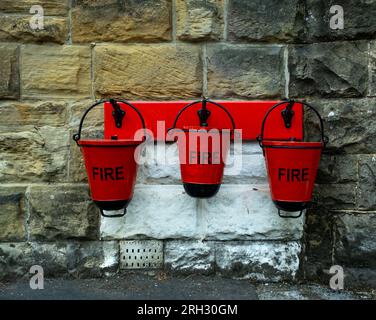 Drei rote Feuereimer aus Metall hängen an der Wand am Bahnhof Goathland der North York Moors Railway Stockfoto
