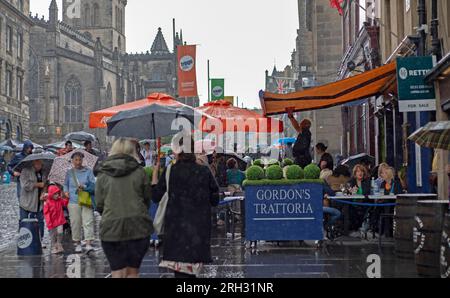 Royal Mile, Edinburgh, Schottland, Großbritannien. 13. August 2023. Die Darsteller des Edinburgh Festival Fringe erlitten heftige Regenschauer während ihrer Shows auf der High Street am zweiten Sonntag des Kunstfestivals, die Brolleys gingen hoch, wasserdichte Dächer waren an und das Publikum blieb größtenteils in der Nähe. Gordons Besitzer Gordons Trattoria versucht nach einer Sintflut einige der Regenwasserpfützen von seinem Dach zu entfernen. Kredit: Archwhite/alamy Live News. Stockfoto