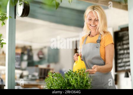 Wunderschöne, Reife Frau, Die Potted Flowers Auf Der Terrasse Im Café Bewässert Stockfoto