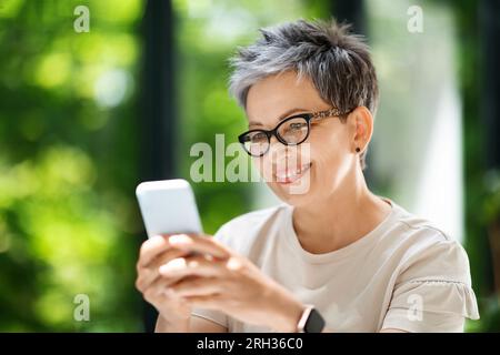 Nahaufnahme einer glücklichen erwachsenen Frau, die am Arbeitsplatz ein Handy benutzt Stockfoto