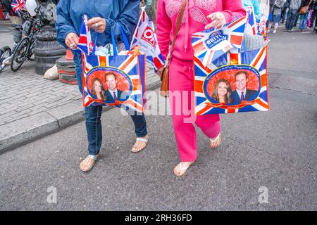 Zwei Personen gehen mit Taschen, die das Porträt von Catherine, Herzogin von Cambridge, und ihrem Ehemann Prinz William, London, Großbritannien zeigen Stockfoto