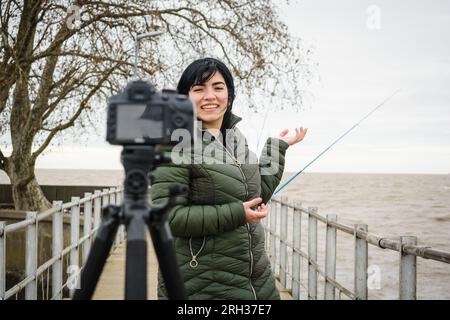 Eine junge venezolanische lateinische Frau, die Content-Ersteller ist, steht auf dem Pier über dem Fluss in buenos aires und macht mit ihrer Kamera Reisevideos für Social medi Stockfoto