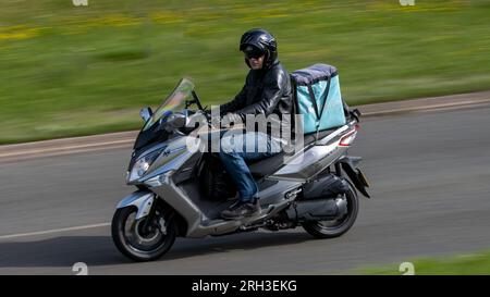 Milton Keynes, Großbritannien - Aug 10. 2023: Deliveroo Rider fährt ein Sym Joymax Motorrad auf einer englischen Landstraße. Stockfoto