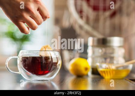 Die Frau legt den Teebeutel in den Glasbecher mit heißem Wasser Stockfoto