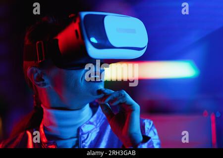 Neon-Metaverse-futuristisches Konzept. Nachdenkliche, moderne Geschäftsfrau mit VR-Headset auf dunklem Hintergrund. Stockfoto