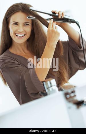 Lächelnden jungen Frau Haarglättung mit Haarglätter Stockfoto