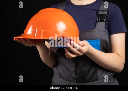 Orangefarbener Schutzhelm in den Händen einer Bastlerin auf schwarzem Hintergrund. Stockfoto