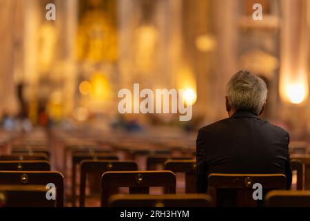 Ein älterer Mann sitzt auf einem Stuhl in einer Kirche. Mitten im Bild Stockfoto