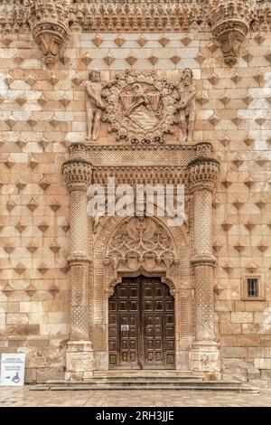 Portal inspiriert von den Mudejar-Palästen des 14. Jahrhunderts, Tür zwischen Säulen, heraldisches Sturzgewölbe, spitzer Bogen und gegenüberliegende Figuren auf den Spandrillen. Stockfoto