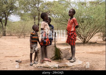 Junge kenianische Jungs stehen an einem Wasserhahn und beschaffen frisches Wasser aus einem nahegelegenen Bohrloch, Baringo County, Kenia Stockfoto