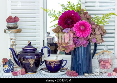 Tischaufteilung mit einer Tasse Kaffee, altem Porzellan und einem Strauß Dahlien und Hortensien Stockfoto