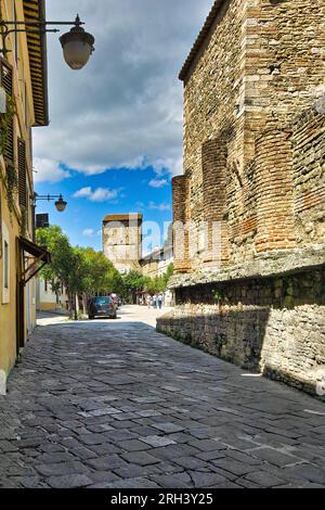 Bevagna Town, Umbrien, Italien. Eine charakteristische gepflasterte Straße mit rechts dem römischen Tempel und im Hintergrund einem mittelalterlichen Turm. Stockfoto