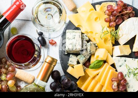 Käseplatte mit handwerklich hergestelltem Käsesortiment und Weingläsern mit weißem Fliesenhintergrund. Stockfoto