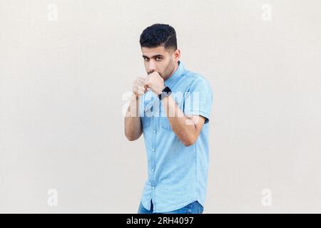Porträt eines aggressiven, wütenden Mannes, der ein Jeansshirt trägt, bereit ist anzugreifen, Hände in der Box hält, in die Kamera schaut, kämpft. Studioaufnahmen im Innenbereich isoliert auf grauem Hintergrund. Stockfoto