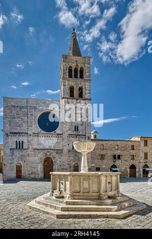 Bevagna, Umbrien, Italien. Der Brunnen aus dem 19. Jahrhundert und die Michaelskirche aus dem 12. Jahrhundert auf der Piazza Silvestri mit blauem Himmel und weißen Wolken. Stockfoto