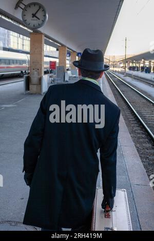 Ein Mann steht mit Koffern auf dem Bahnsteig und kümmert sich um die Ankunft des Zuges Stockfoto