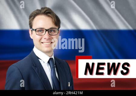 Nachrichtensprecher, erzählt die neuesten Nachrichten, lächelnd, vor dem Hintergrund der russischen Flagge. Medien und Propaganda. Stockfoto