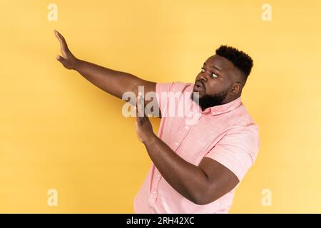 Nein, es ist beängstigend. Seitenansicht eines verängstigten, geschossenen Mannes, der ein rosa Hemd trägt, sich vor Angst die Hände hebt, entsetzt und panisch aussieht, sich vor Phobie versteckt. Innenstudio-Aufnahme isoliert auf gelbem Hintergrund. Stockfoto