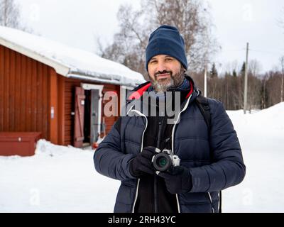 Porträt eines männlichen Fotografen, der in einer verschneiten Landschaft in einer schwedischen Stadt in die Kamera schaut Stockfoto