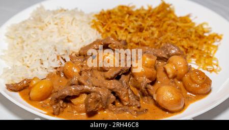 Traditionelles Filet Mignon Stroganoff, serviert auf einem weißen Teller mit Reis und Pommes frites Stockfoto