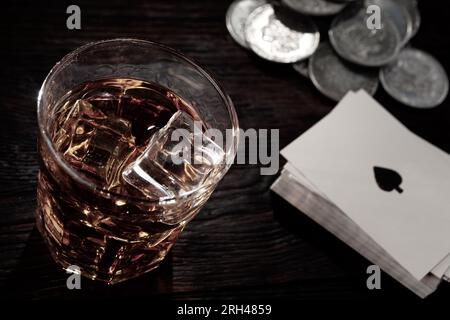 Glücksspiel im Wilden Westen. Silbermünzen, Spielkarten und Whiskey auf einem Holztisch. Stockfoto