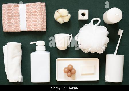 Weiß-pinkfarbenes Objekt im Badezimmer. Duschtuch, Baumwollblume, Halter, Kerze, Shampoo-Spender, tasse, Puffer, Seife, Zahnbürste auf grünem Stoffhintergrund Stockfoto