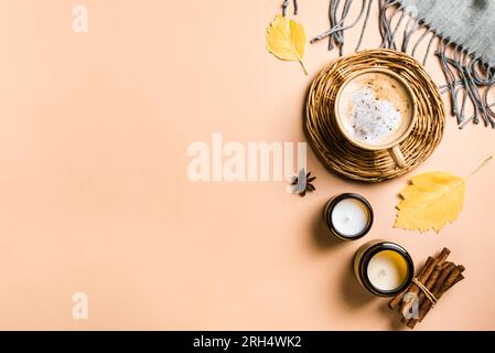 Herbstblätter und eine Tasse Cappuccino-Kaffee, kreativ, flach liegend. Hintergrundinformationen. Getrocknete Blätter, Kerzen und Kaffee auf beigefarbenem Schreibtisch, Hygge-gemütliches Konzept, Bulle Stockfoto