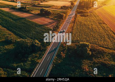 Luftaufnahme des Verkehrs auf der Landstraße bei Sonnenuntergang im Sommer, Dröhnensicht aus dem Blickwinkel pov Bild von Autos, die entlang der Autobahn durch die Vojvodina in SE fahren Stockfoto